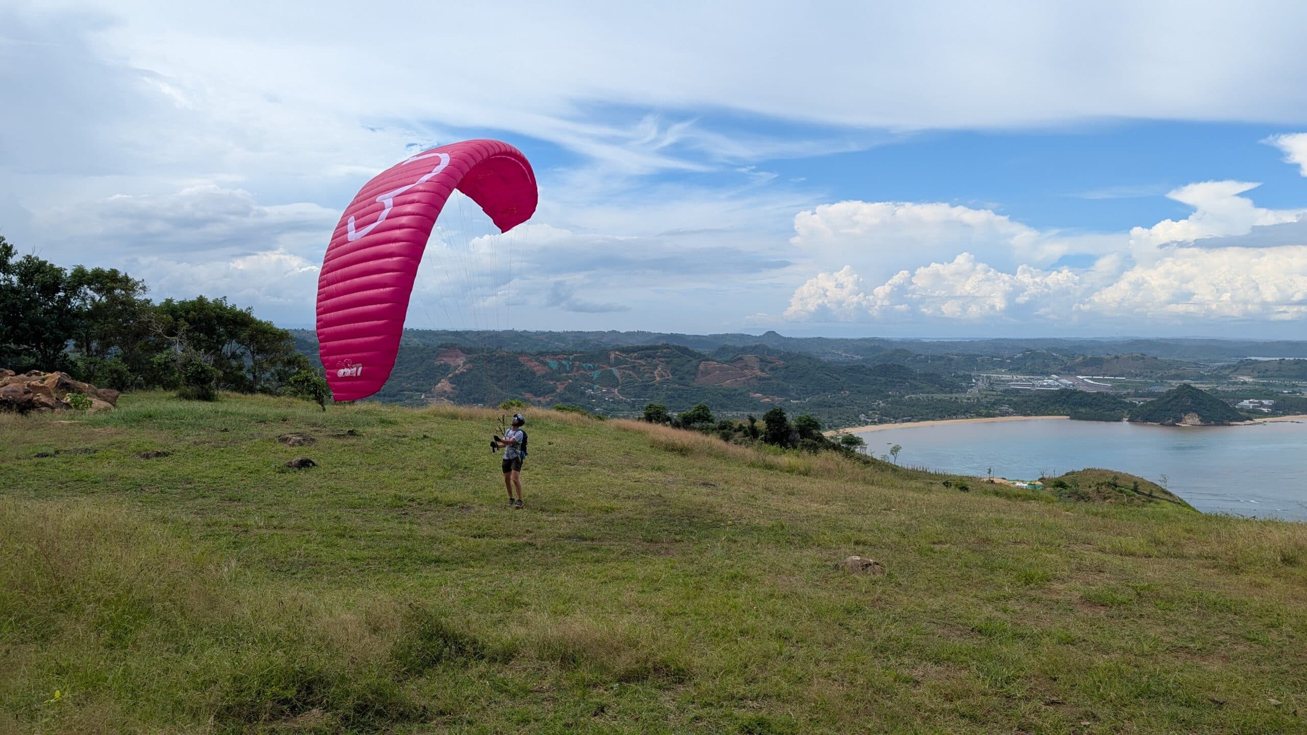 Eine Person übt das Groundhandling mit einem pinken Gleitschirm vom Typ LittleCloud Superfly am Startplatz Prabu Hill über der Küste von Lombok.