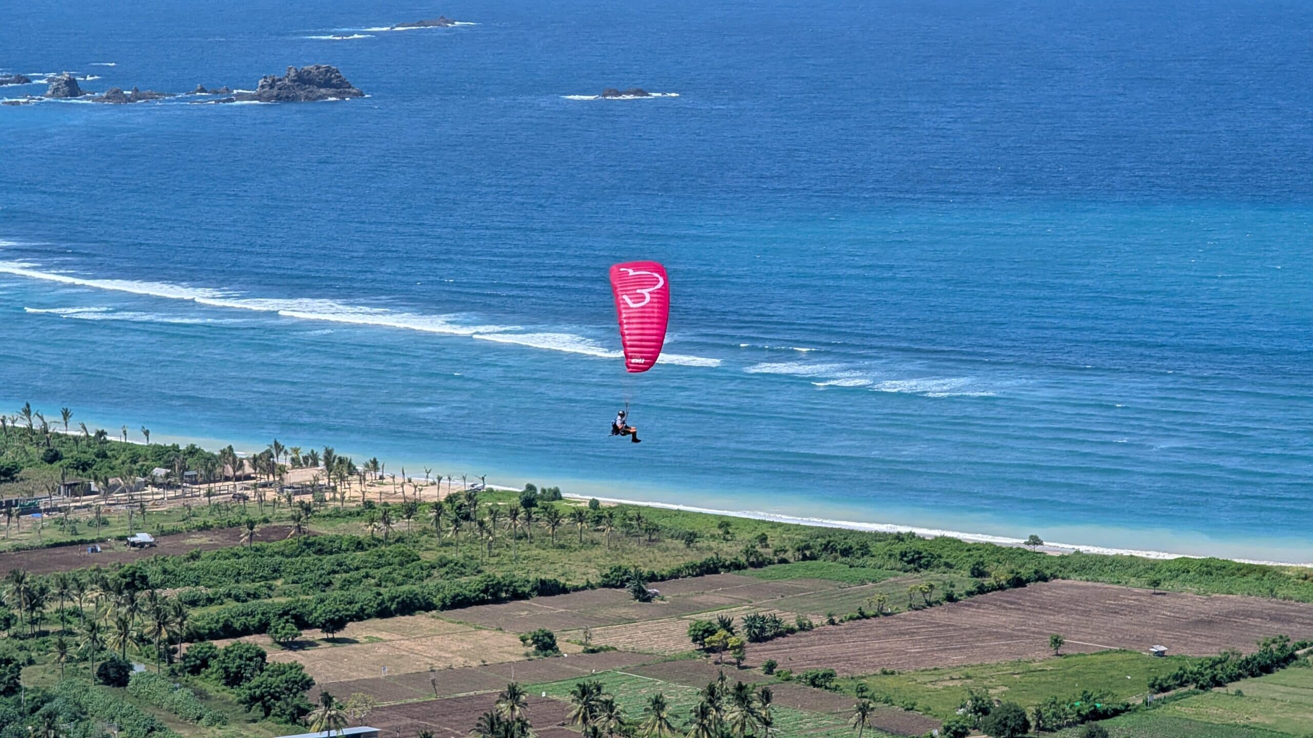 Ein pinker LittleCloud Superfly Gleitschirm beim Soaring über der Küste von Lombok mit Blick auf das blaue Meer.